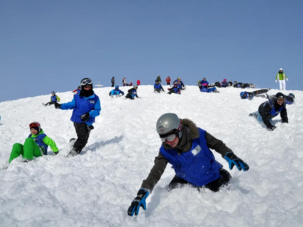 Jugendliche liegen und sitzen ausgelassen auf einer Schneekuppe.